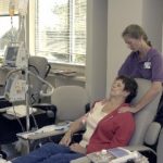 Oncology massage therapist standing behind seated patient giving a shoulder massage.